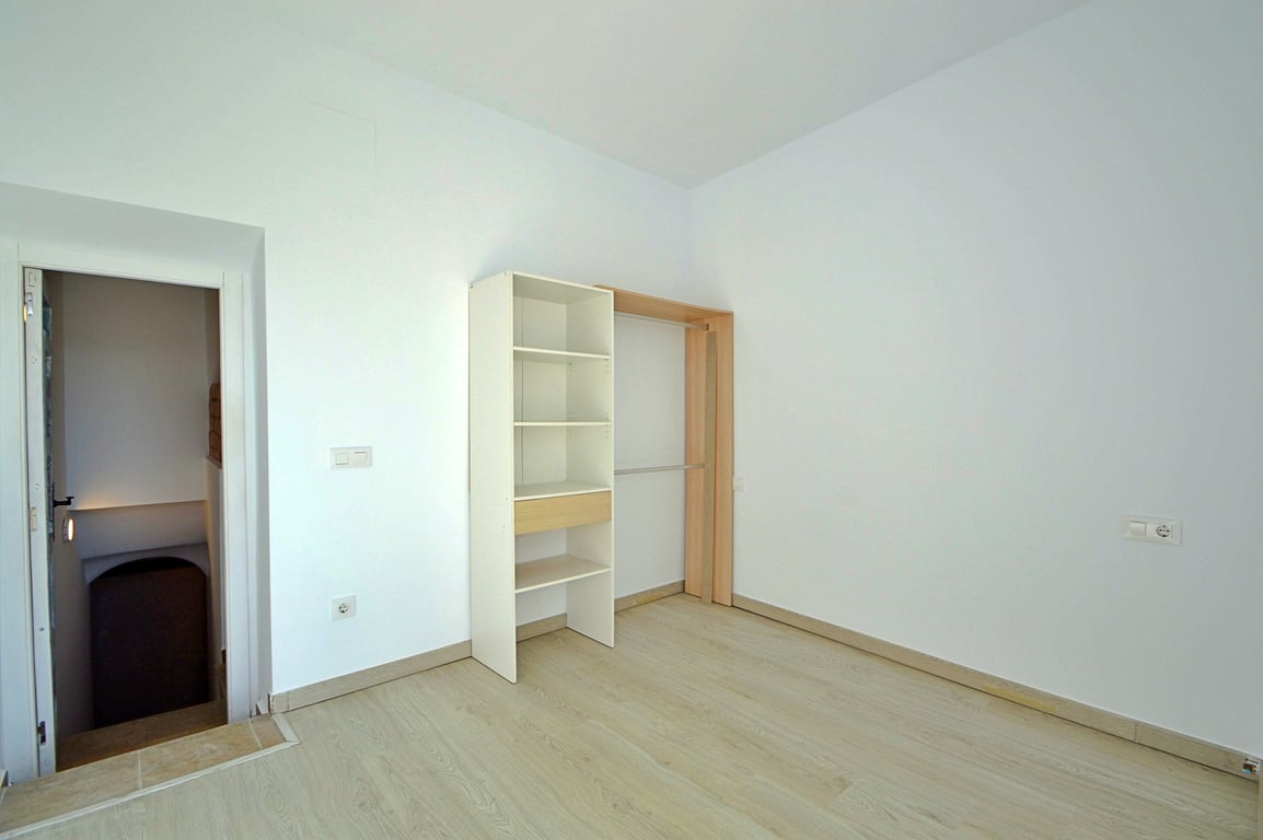 Veelzijdige kamer met houtlook vloer, witte muren en een open kast met hanggedeelte, gelegen naast de toegang tot de trap.
