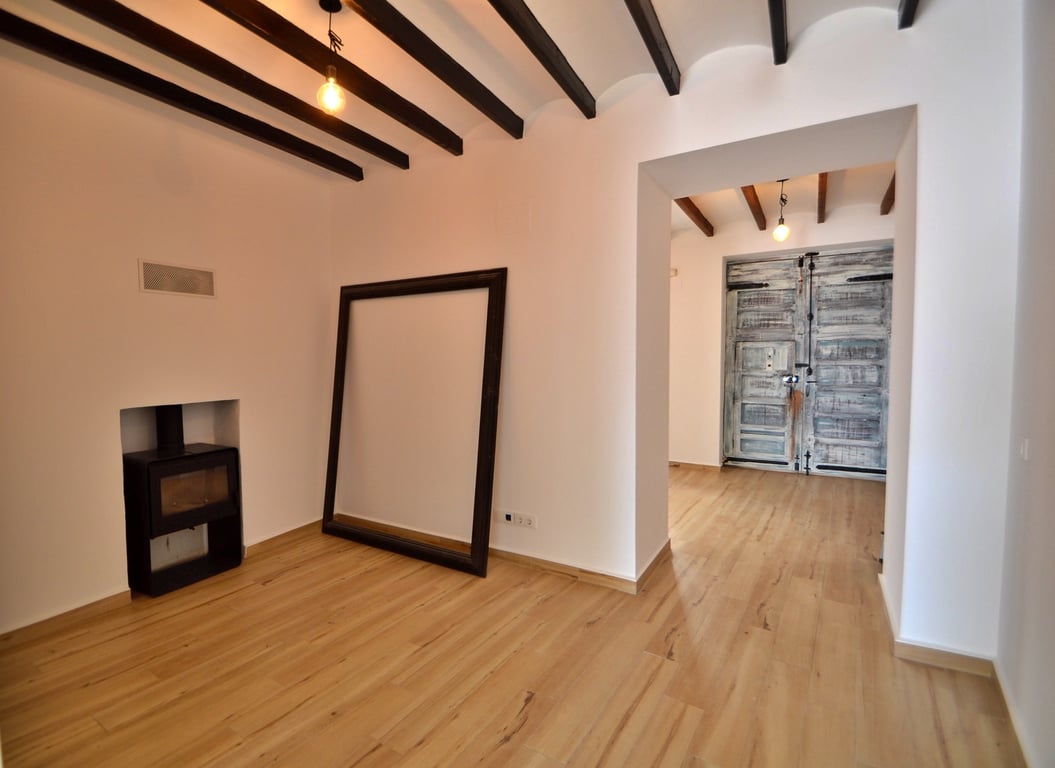 Woonkamer met zichtbare houten balken, een ingebouwde houtkachel en lichte vloeren. Een gerestaureerde rustieke deur vormt een authentiek detail in de woning.
