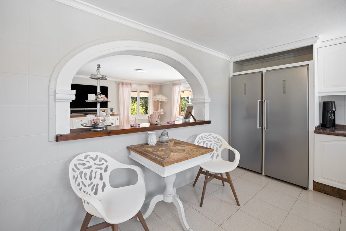 Keuken met een open boogverbinding naar de woonkamer, voorzien van een dubbele rvs-koelkast en een ontbijthoek met houten tafel en moderne stoelen.