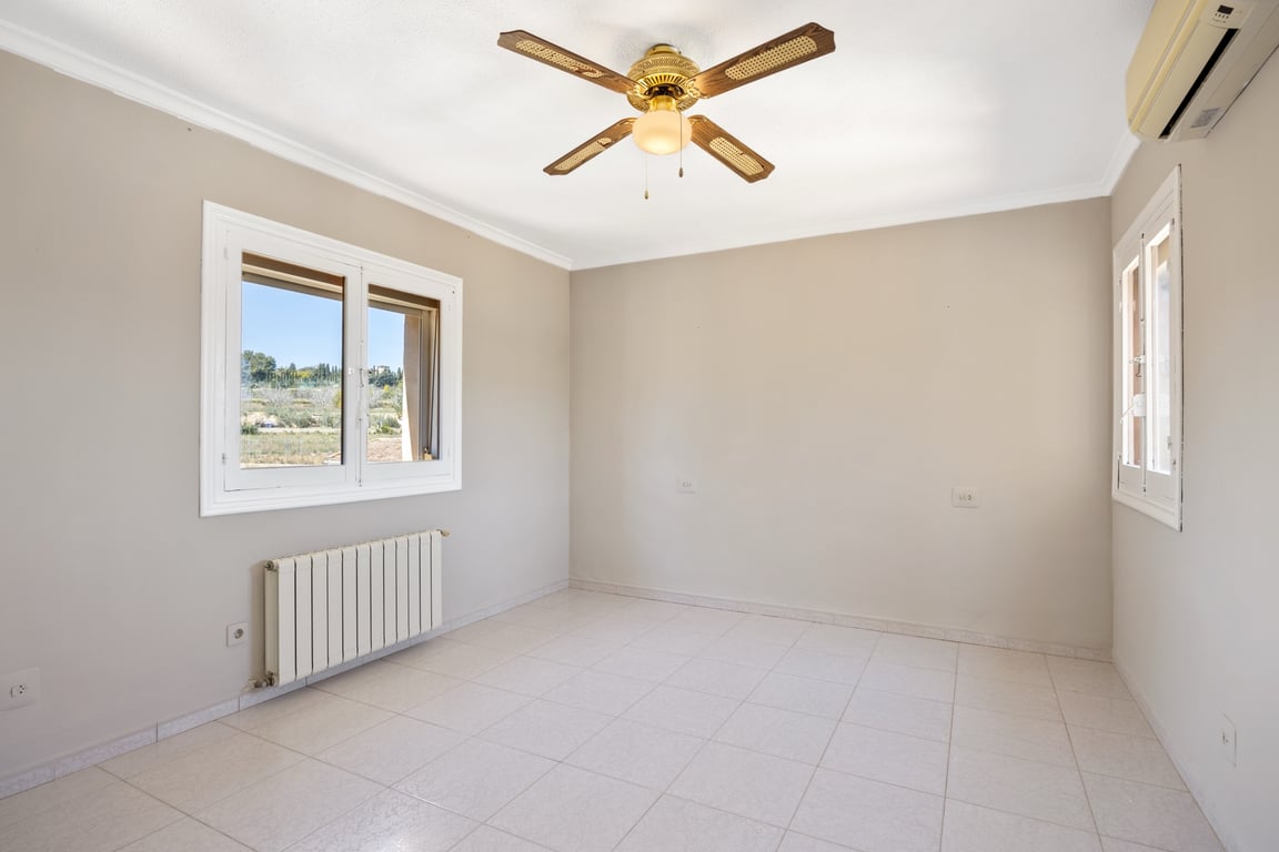 Lichte slaapkamer met tegelvloer, klassieke plafondventilator, airconditioning en radiator. De ramen bieden een vrij uitzicht op de natuurlijke omgeving van de villa.