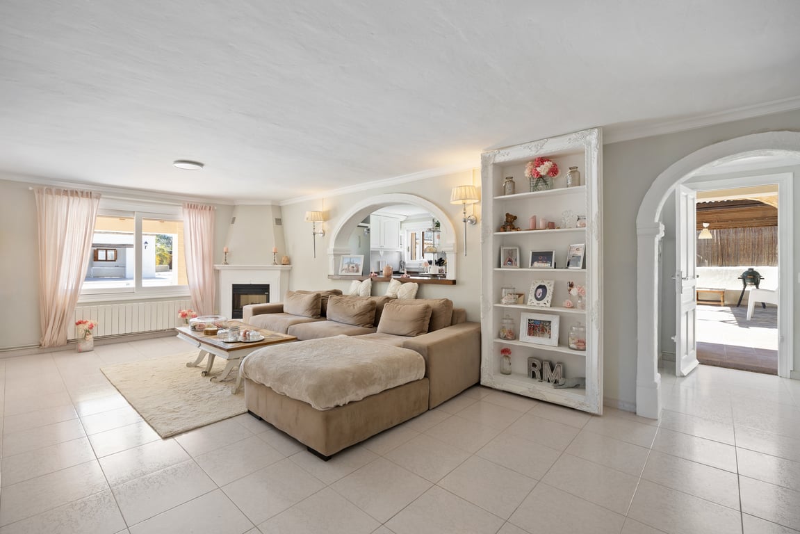 Lichte woonkamer met hoekhaard, modulaire bank en boogopeningen naar de keuken en het terras. Voorzien van een decoratieve wandkast en een lichte tegelvloer.