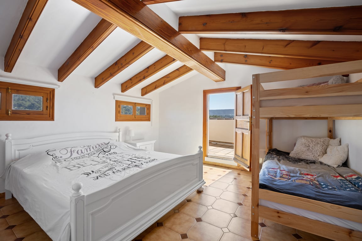 Slaapkamer op de zolderverdieping met houten balkenplafond, terracotta vloertegels en toegang tot een privéterras. Voorzien van een tweepersoonsbed en een houten stapelbed.
