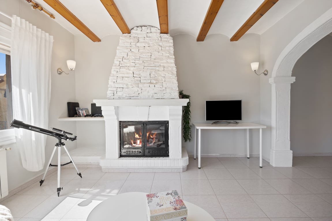 Woonkamer met een witte stenen open haard, houten plafondbalken en een traditionele stenen boog die de ruimtes met elkaar verbindt.