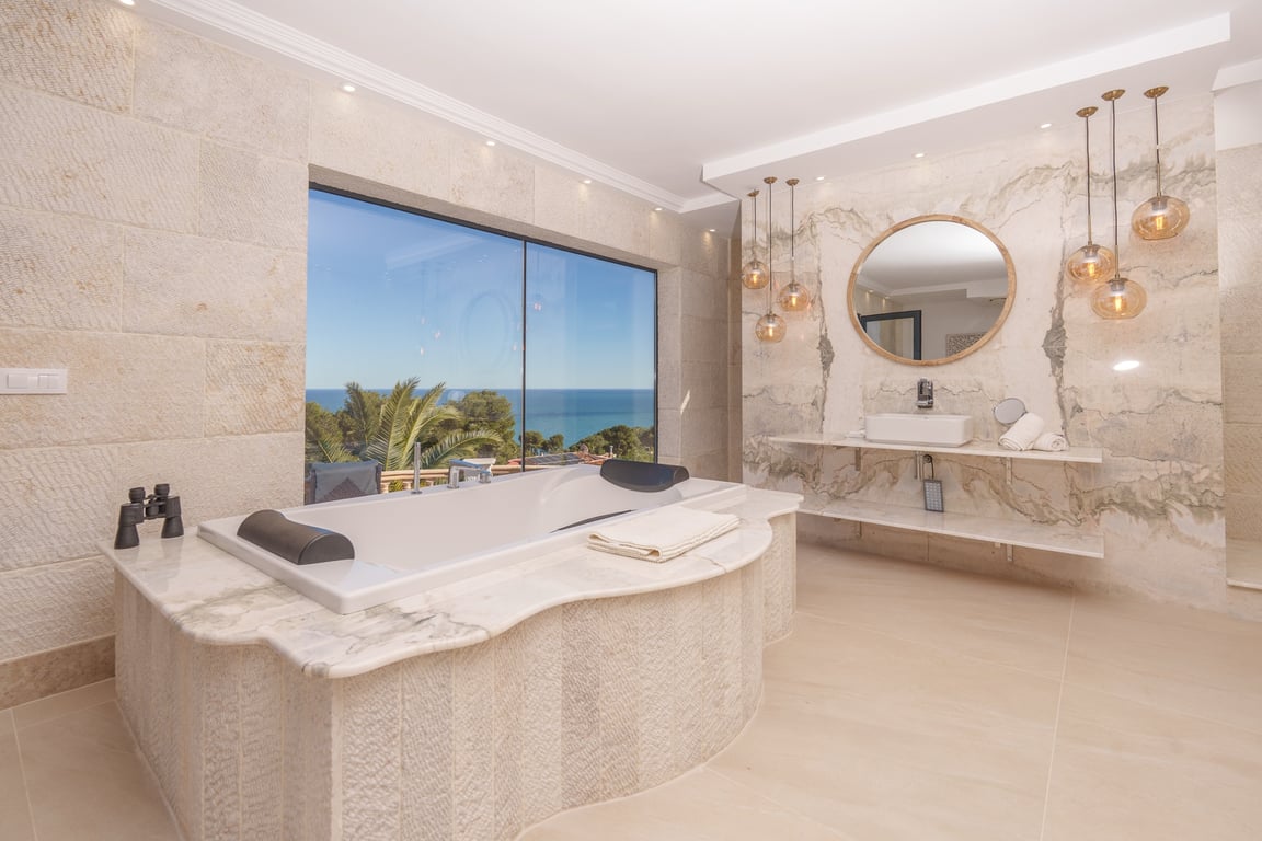 Badkamer van de master suite met een marmeren ligbad, muren van kalksteen en een groot raam met vrij uitzicht op de Middellandse Zee.