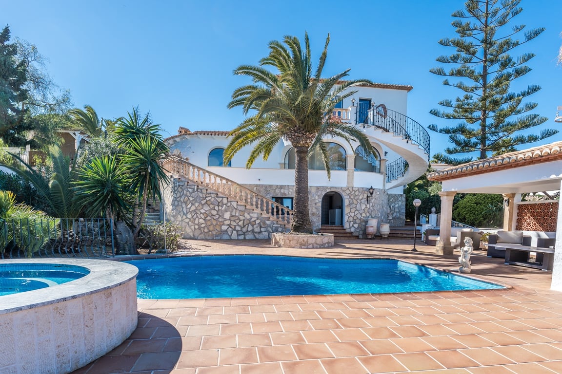 Buitenaanzicht met zwembad, ronde jacuzzi en natuurstenen gevel. Een karakteristieke wenteltrap verbindt de terrassen in een volgroeide mediterrane tuin.