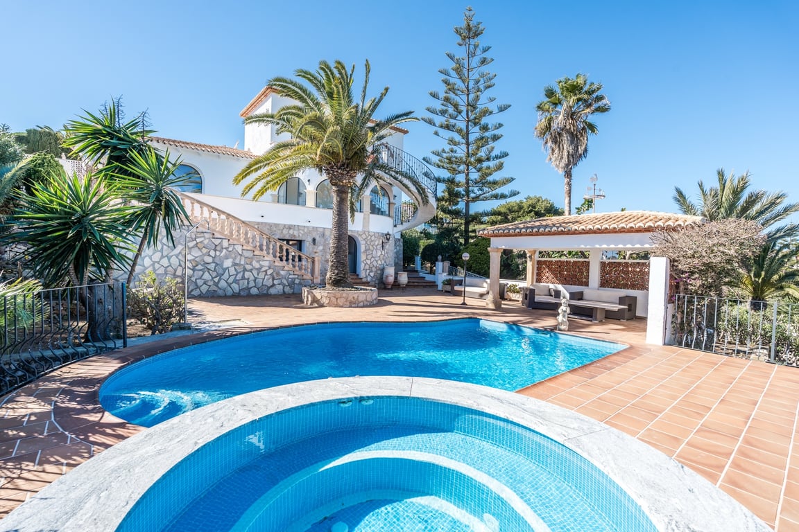 Buitenaanzicht van het zwembad en de ronde jacuzzi op een terracotta terras, met de stenen gevel van de villa en mediterrane palmen op de achtergrond.