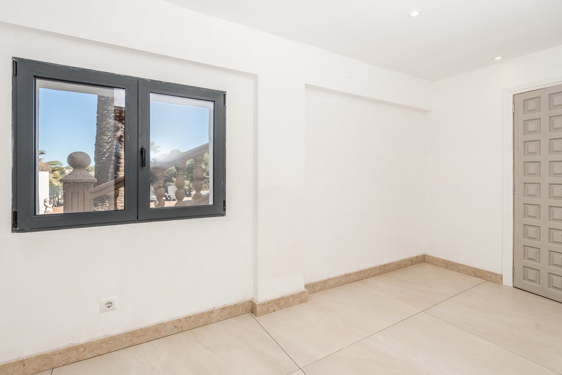 Gerenoveerde kamer met natuurstenen vloer, inbouwspots en een donker aluminium raam met uitzicht op de mediterrane buitenruimte.