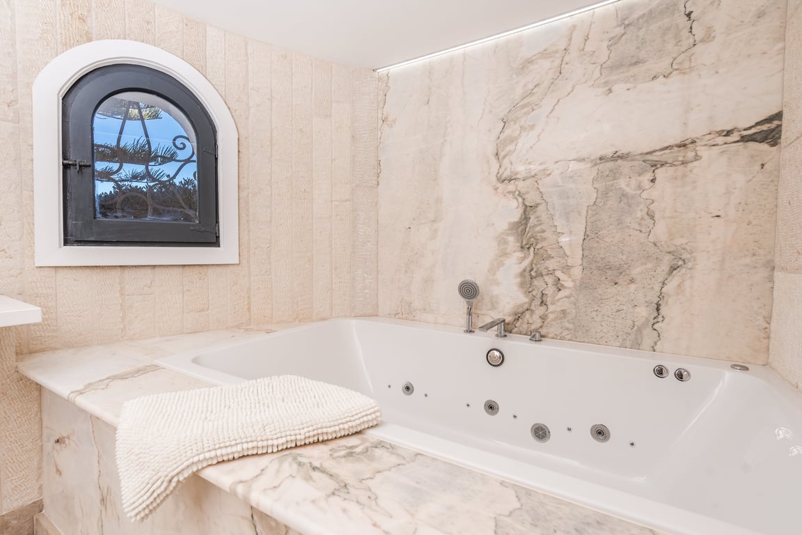 Ingebouwd hydromassagebad met marmeren afwerking, natuurstenen wanden en een authentiek boograam met smeedwerk.