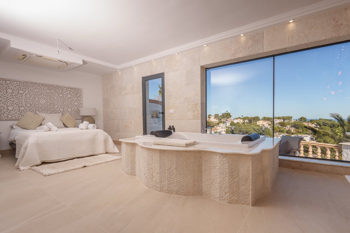 Master suite met een geïntegreerd bad bekleed met natuursteen, grote ramen met uitzicht op zee en een rustgevend open ontwerp.
