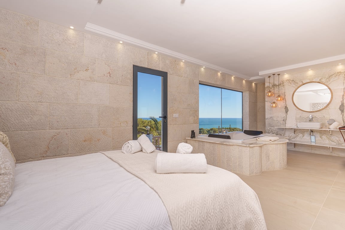 Master suite met natuurstenen muren, geïntegreerde jacuzzi bij het raam met zeezicht en een open badkamer met marmeren details.
