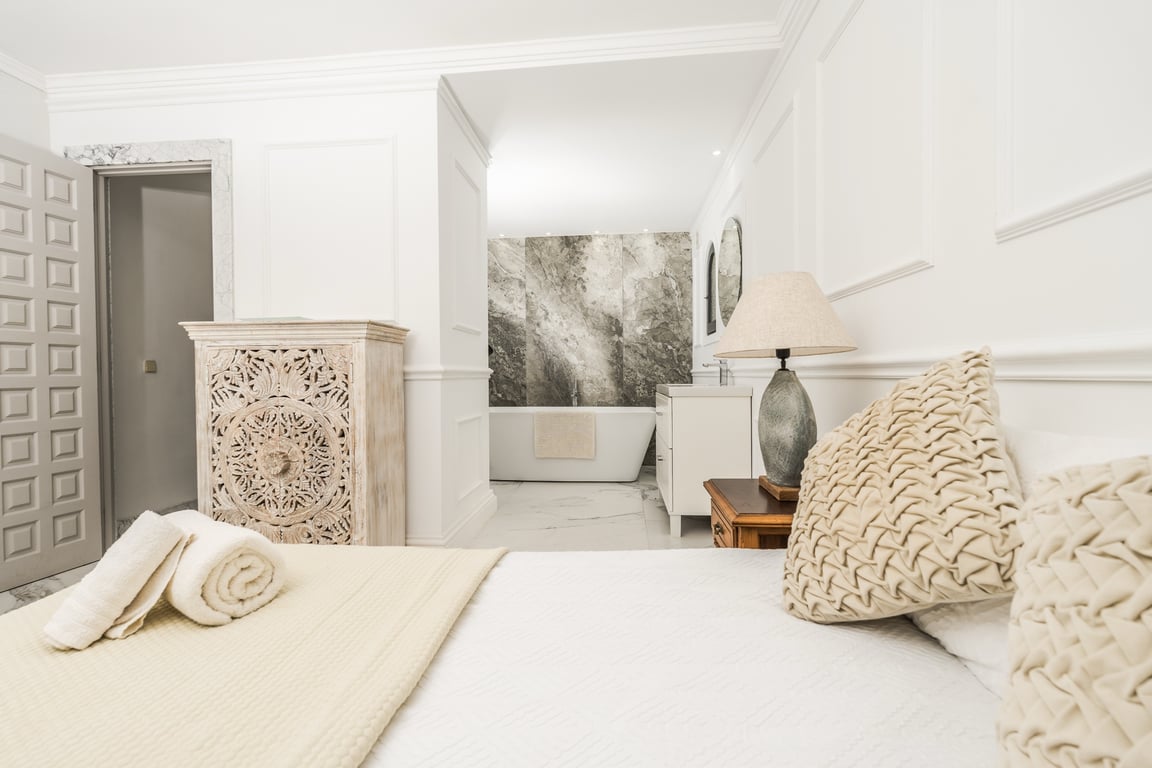 Master suite met open badkamerconcept, vrijstaand ligbad voor een marmeren wand en verfijnde wandpanelen met sierlijsten.