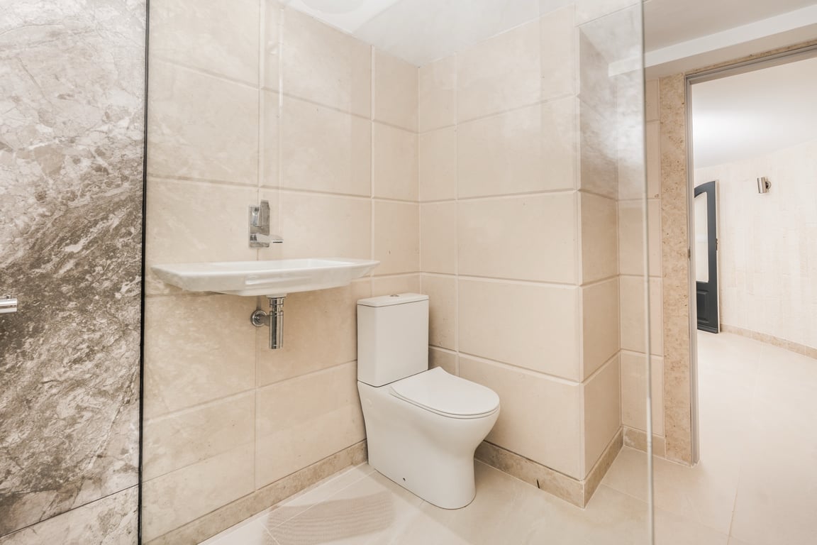 Moderne badkamer met crèmekleurige kalksteenlook tegels, een eigentijds toilet en een zwevende wastafel. Voorzien van een glazen douchewand en marmeren details.