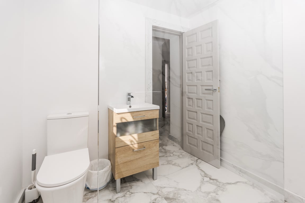 Moderne badkamer met wit marmeren tegels, een licht houten wastafelmeubel en een glazen douchewand voor een heldere uitstraling.