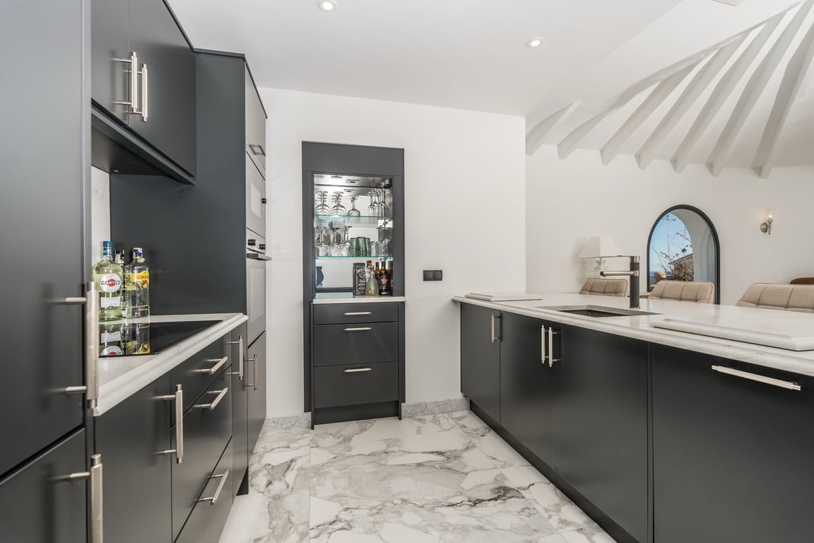 Moderne keuken met donkere kasten, marmeren werkbladen en een centraal eiland. Voorzien van een ingebouwde bar en een uniek plafond met radiale witte balken.