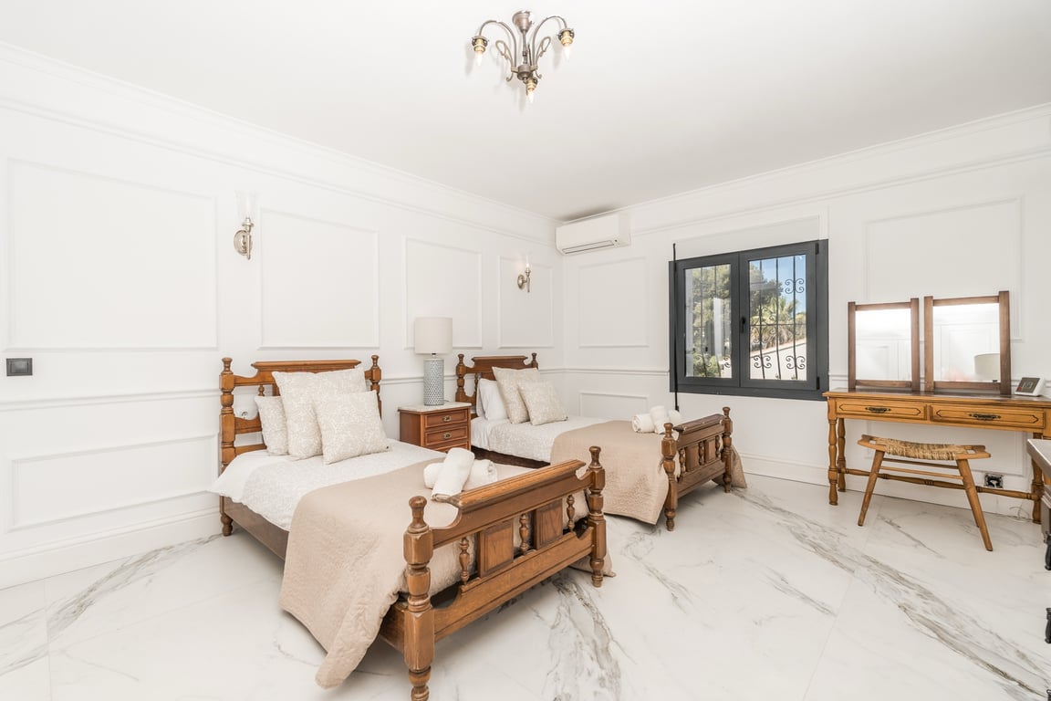Slaapkamer met twee gesneden houten eenpersoonsbedden, marmeren vloer en klassieke wandlijsten. Voorzien van een houten kaptafel en airconditioning.