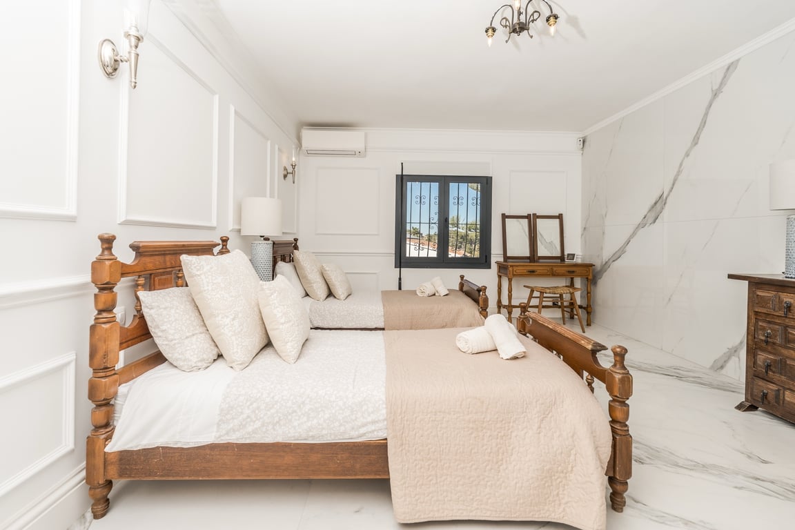 Slaapkamer met twee houten bedden, marmeren vloeren en klassieke wandlijsten. Voorzien van een houten kaptafel en airconditioning.