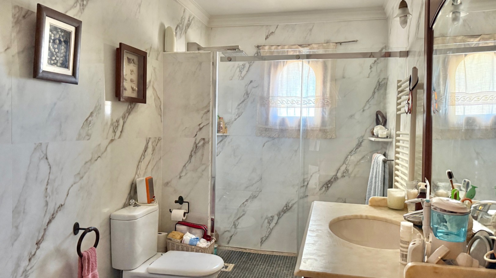 Badkamer met wandtegels in marmerlook, een inloopdouche met glazen wand en een klein boogvenster voor natuurlijke lichtinval.