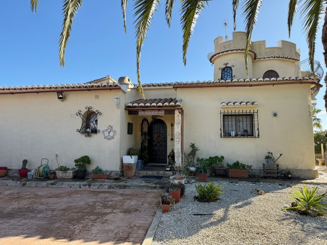 Buitenaanzicht van de villa met een karakteristieke kanteeltoren, boogramen met smeedijzeren tralies en een houten entree omringd door mediterrane planten.