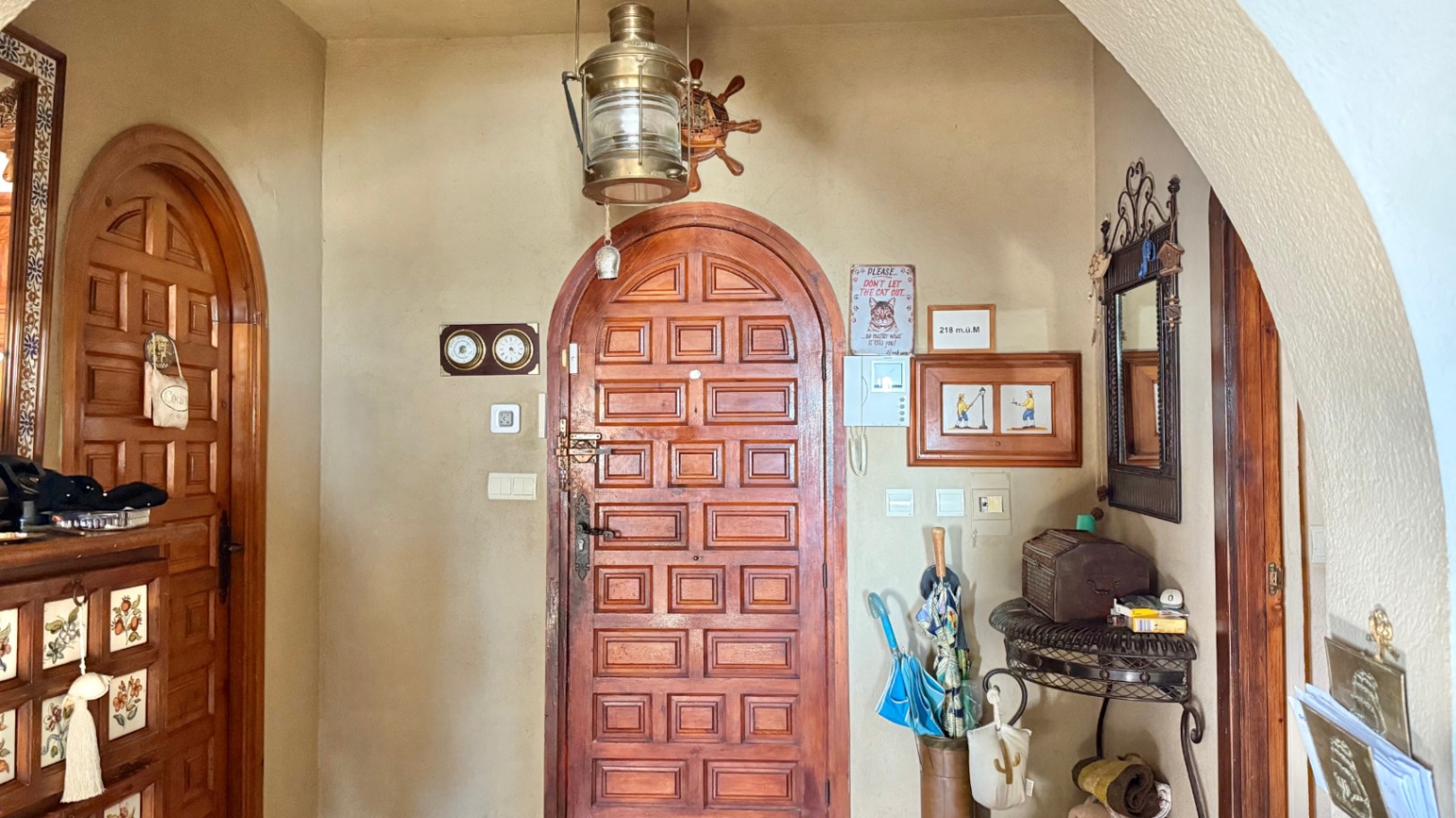 Entreehal met massief houten boogdeuren, nautische decoratie met een koperen lantaarn en smeedijzeren meubilair tegen traditionele gestuukte wanden.
