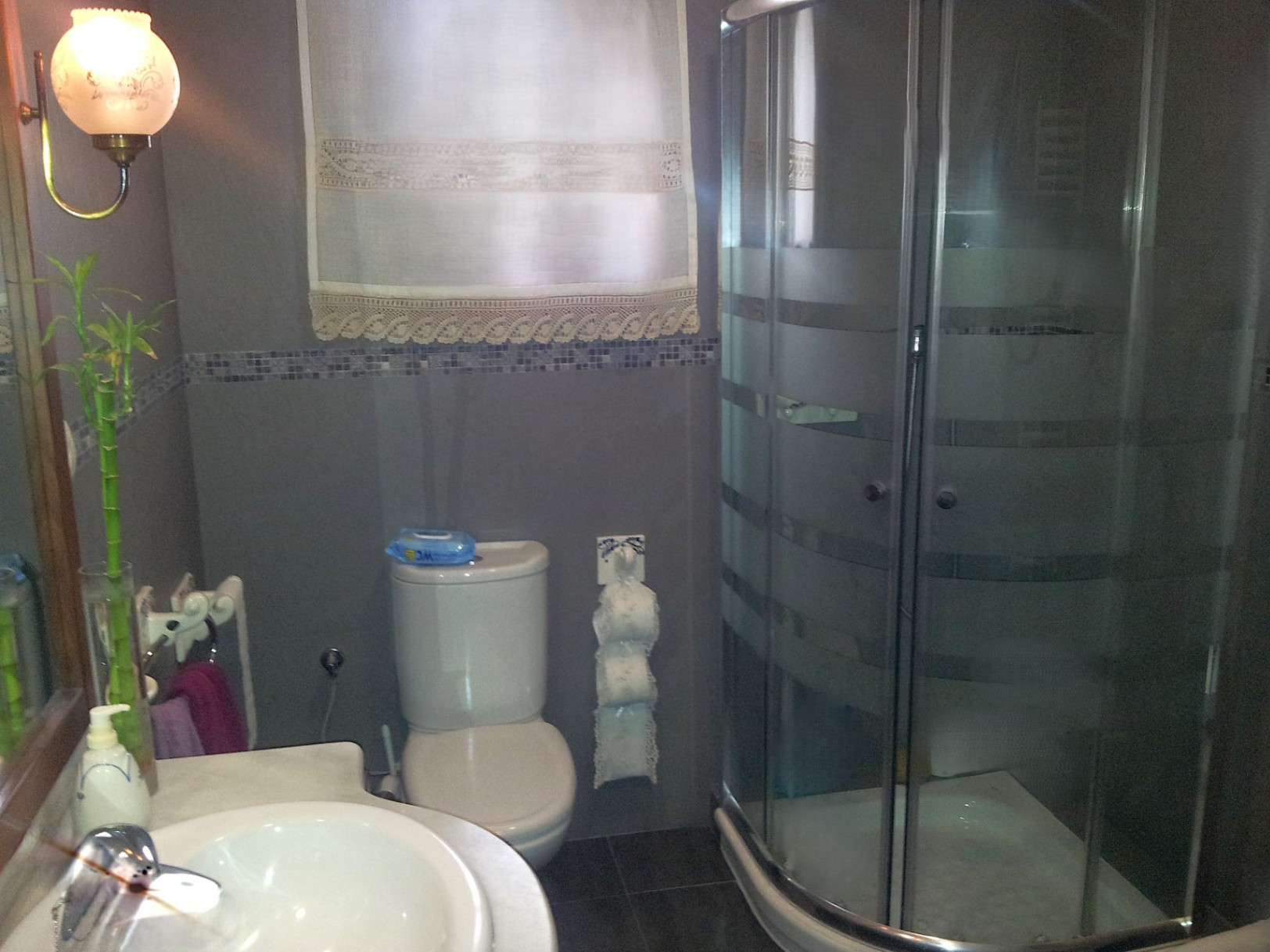 Functionele badkamer met een halfronde hoekdouche, marmeren wastafelblad en grijze wandtegels met een mozaïekrand.