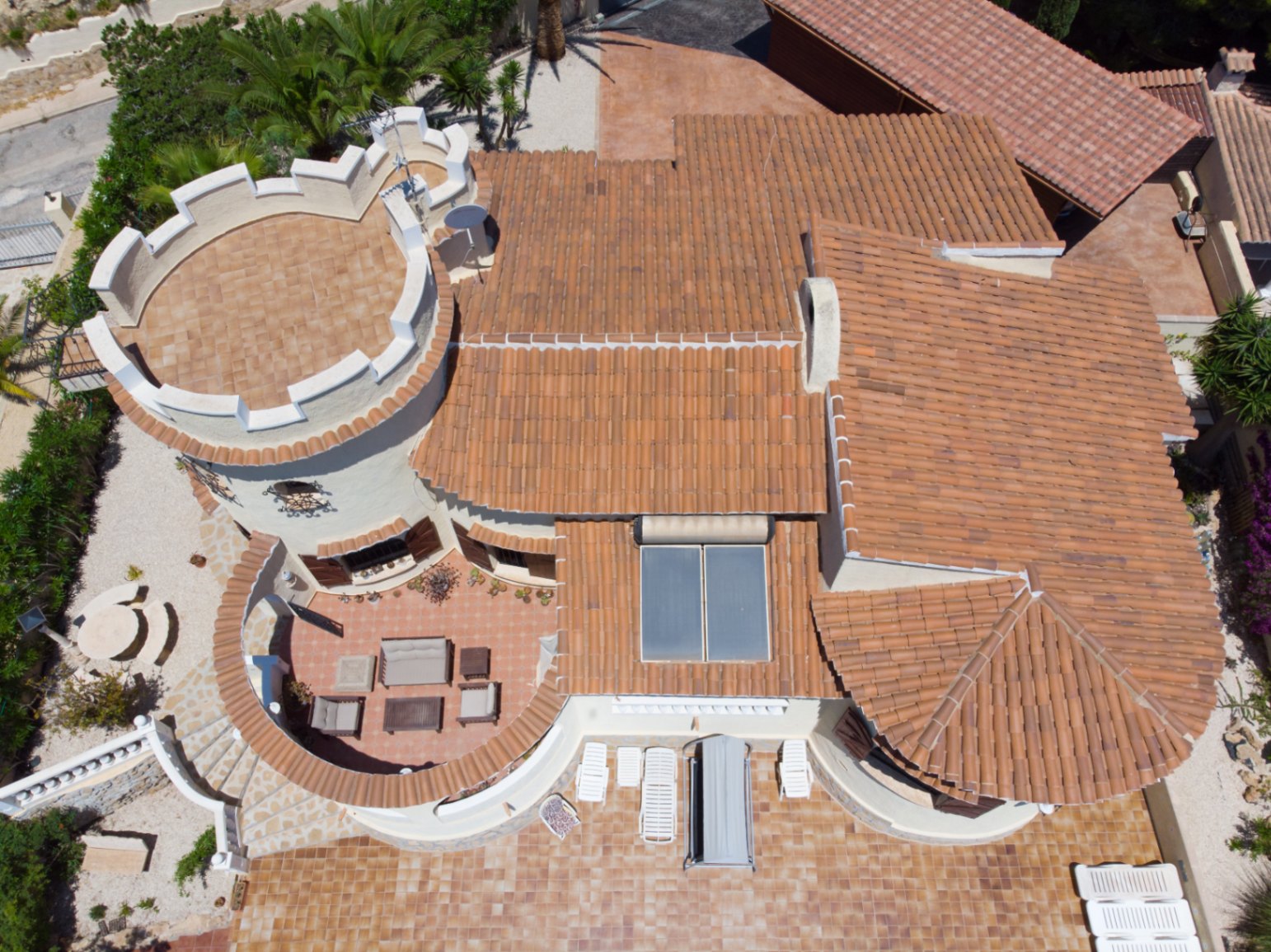 Luchtfoto van de villa met de karakteristieke toren met kantelen, terracotta pannendaken met zonnepanelen en diverse gemeubileerde buitenterrassen.