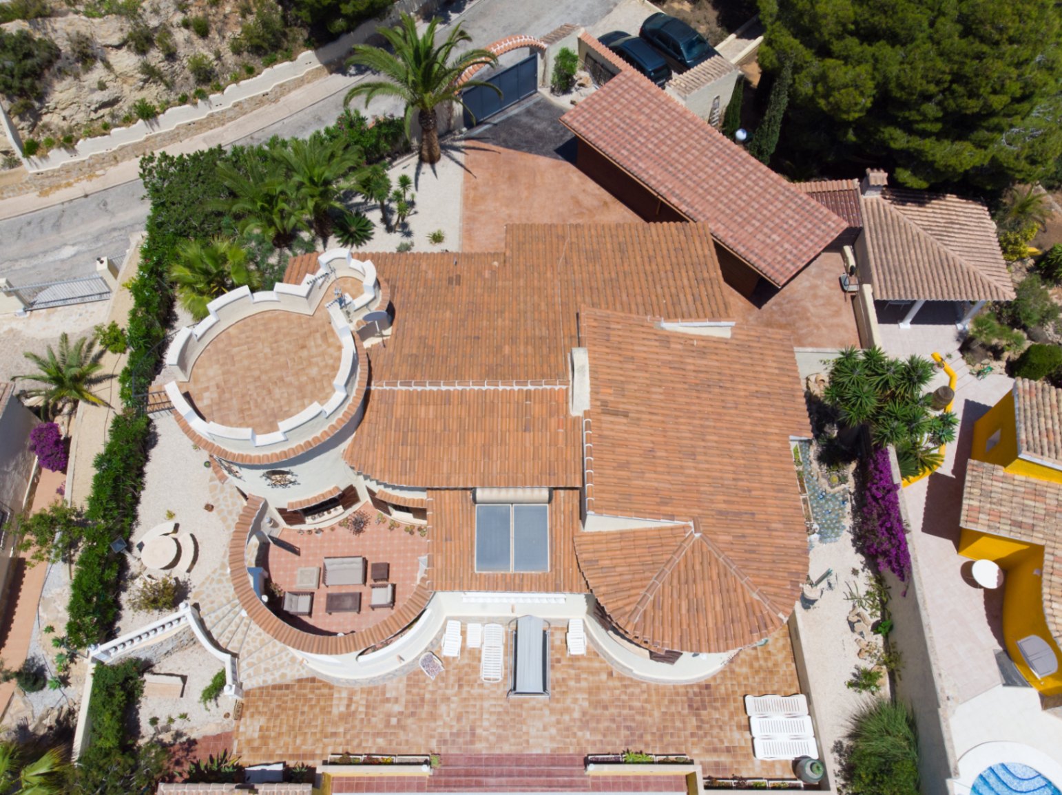Luchtfoto van de villa met mediterrane architectuur, terracotta daken, een karakteristieke ronde toren, zonnepanelen en ruime betegelde terrassen.