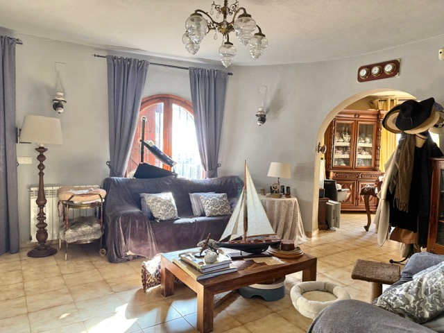 Ronde woonkamer met tegelvloer, een houten boograam en een doorgang naar de eetkamer, ingericht met nautische details en klassieke verlichting.