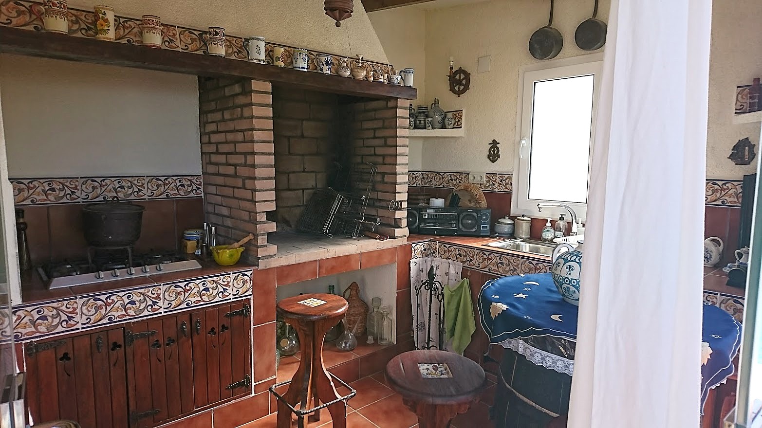 Rustieke buitenkeuken met een ingebouwde bakstenen barbecue, traditionele tegels, een gaskookplaat en houten kasten in Spaanse stijl.