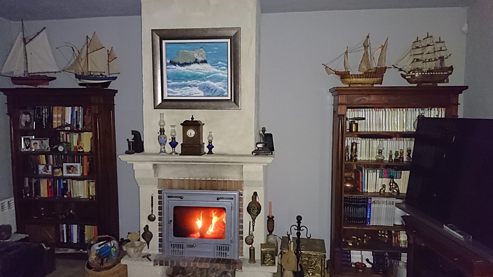 Traditionele woonkamer met een ingebouwde open haard, geflankeerd door klassieke houten boekenkasten en gedecoreerd met scheepsmodellen en maritieme kunst.