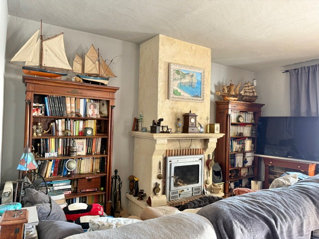 Traditionele woonkamer met een stenen open haard met inzetkachel, geflankeerd door klassieke houten boekenkasten met nautische decoratie en boeken.