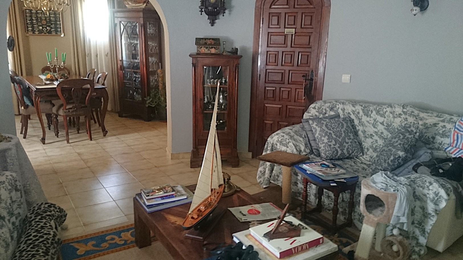 Traditionele woonkamer met tegelvloer, klassiek houten meubilair en een boog die toegang biedt tot de aparte eetkamer met massief houten eethoek.