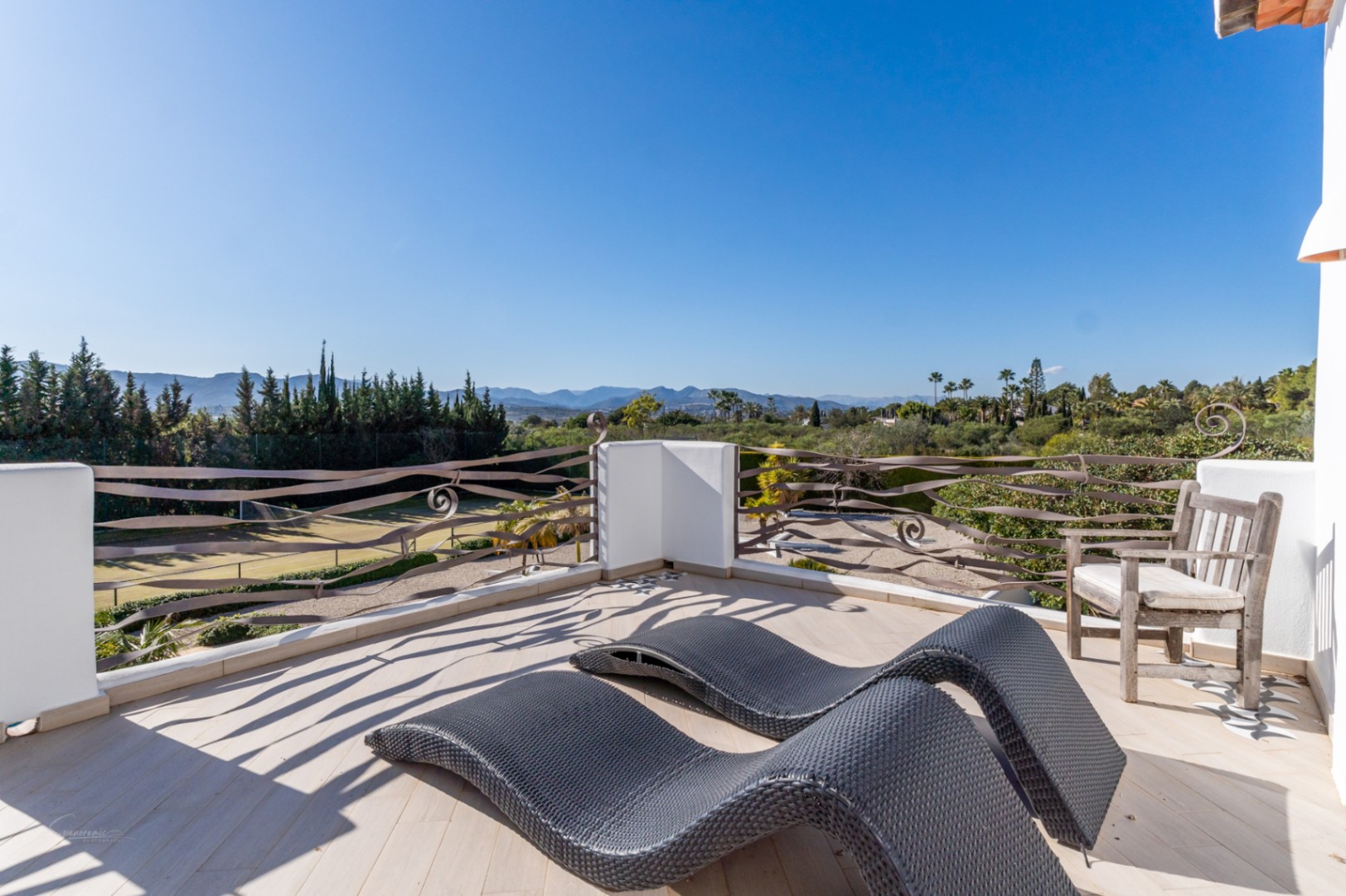Bovenste terras met ergonomische ligbedden en decoratieve ijzeren balustrades, met uitzicht op de tennisbaan en het omliggende Montgó-gebergte.