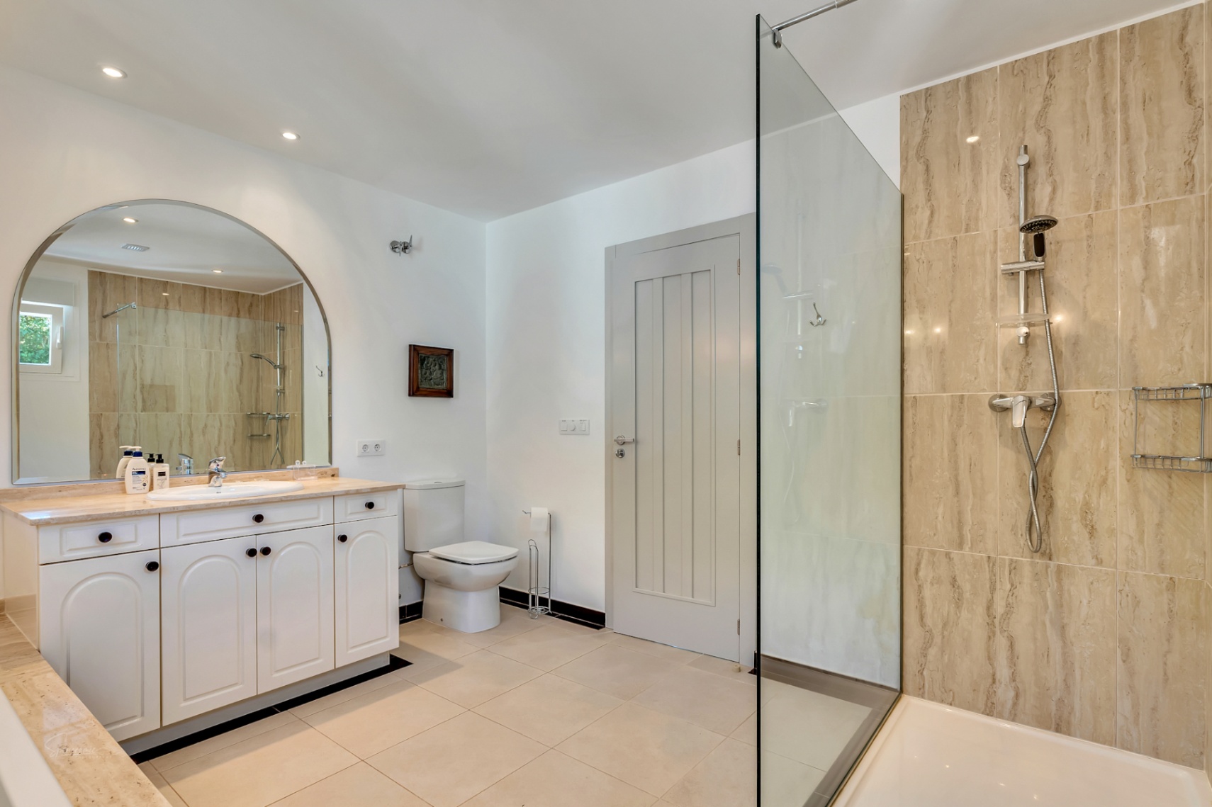 Elegante badkamer met een inloopdouche afgewerkt in natuursteen, wit wastafelmeubel met marmeren blad en een grote boogvormige spiegel.