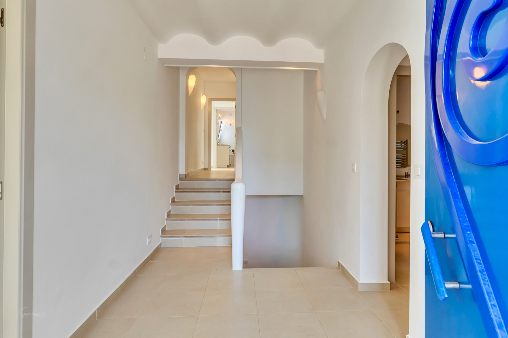Entreehal met een opvallende blauwe designdeur, geschulpte plafonddetails en betegelde trappen die de twee verdiepingen van de villa verbinden.