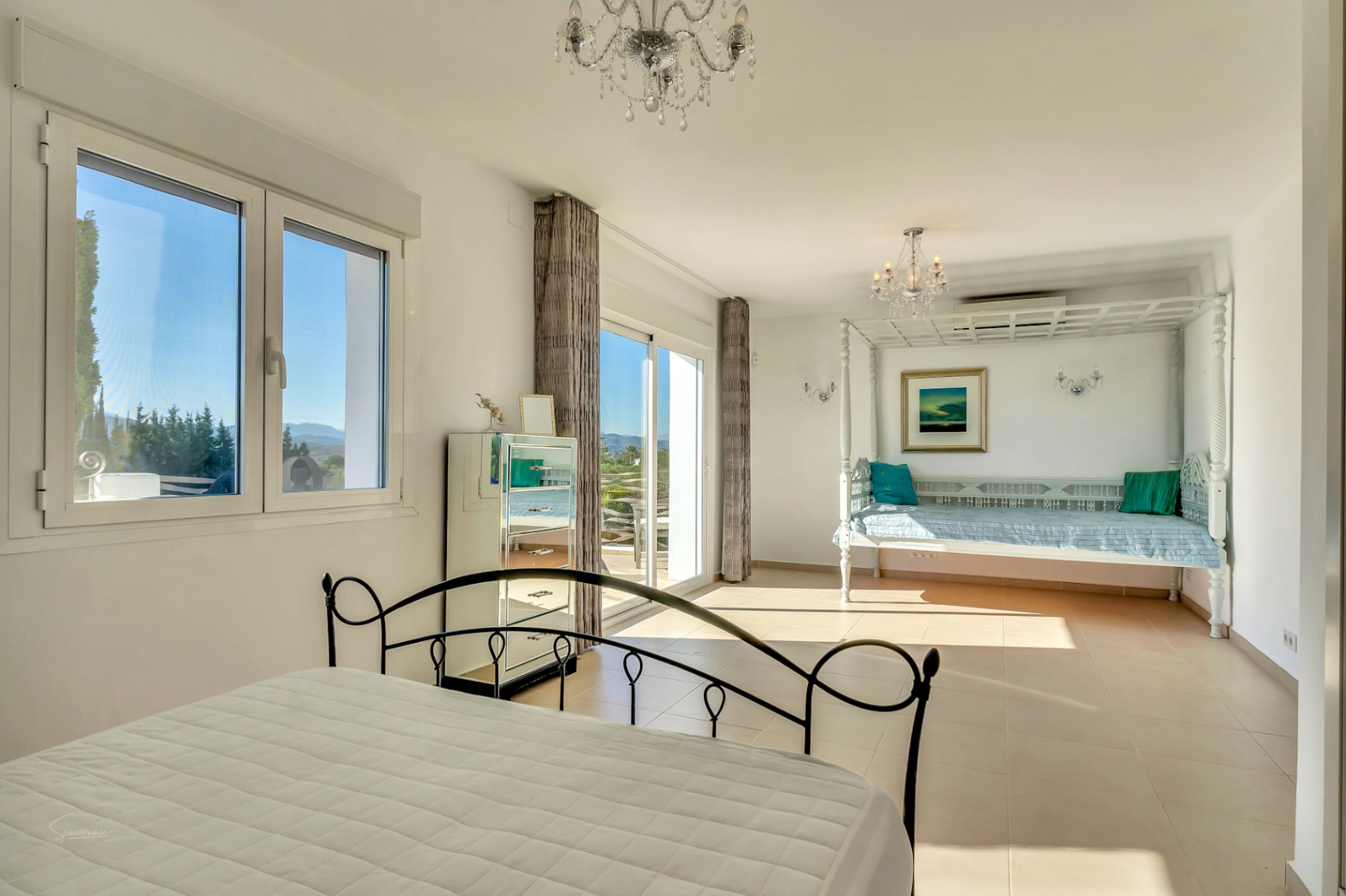 Lichte hoofdslaapkamer met smeedijzeren bed, een wit houten dagbed en schuifdeuren naar het terras met uitzicht op de Montgó-berg.