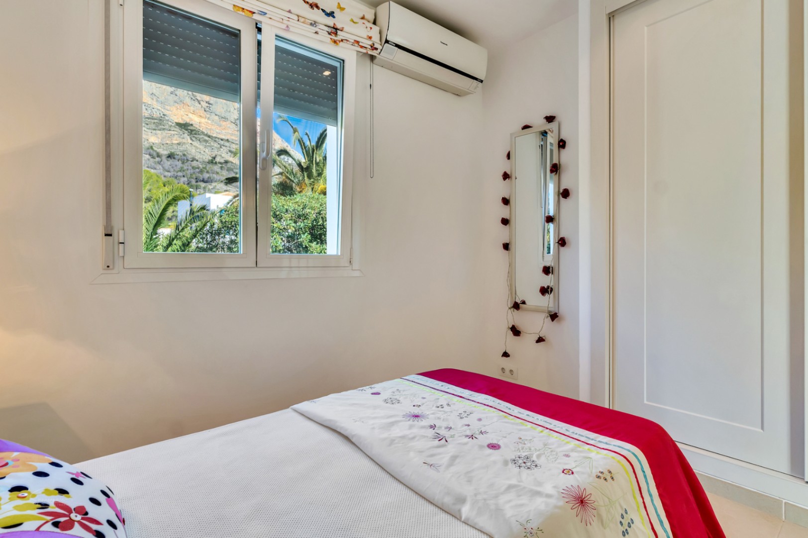 Lichte slaapkamer met inbouwkast, airconditioning en een raam met uitzicht op de Montgó-berg en de omliggende mediterrane beplanting.