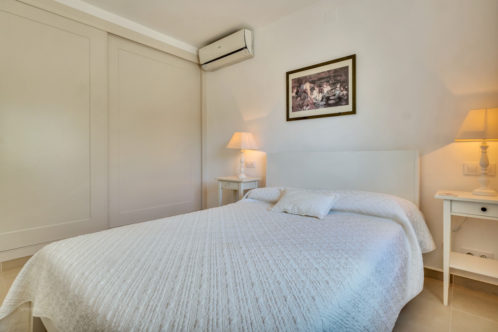 Lichte slaapkamer voorzien van een grote inbouwkast met schuifdeuren, airconditioning en witte nachtkastjes met sfeervolle verlichting.