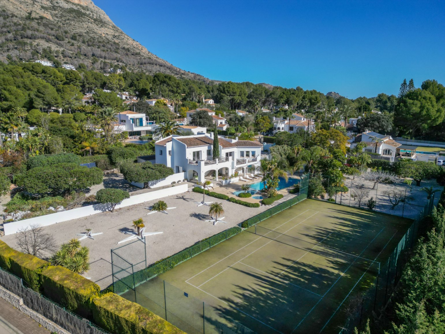 Luchtfoto van de villa in Ibiza-stijl met privétennisbaan, zwembad met jacuzzi en aangelegde tuin aan de voet van de berg Montgó.