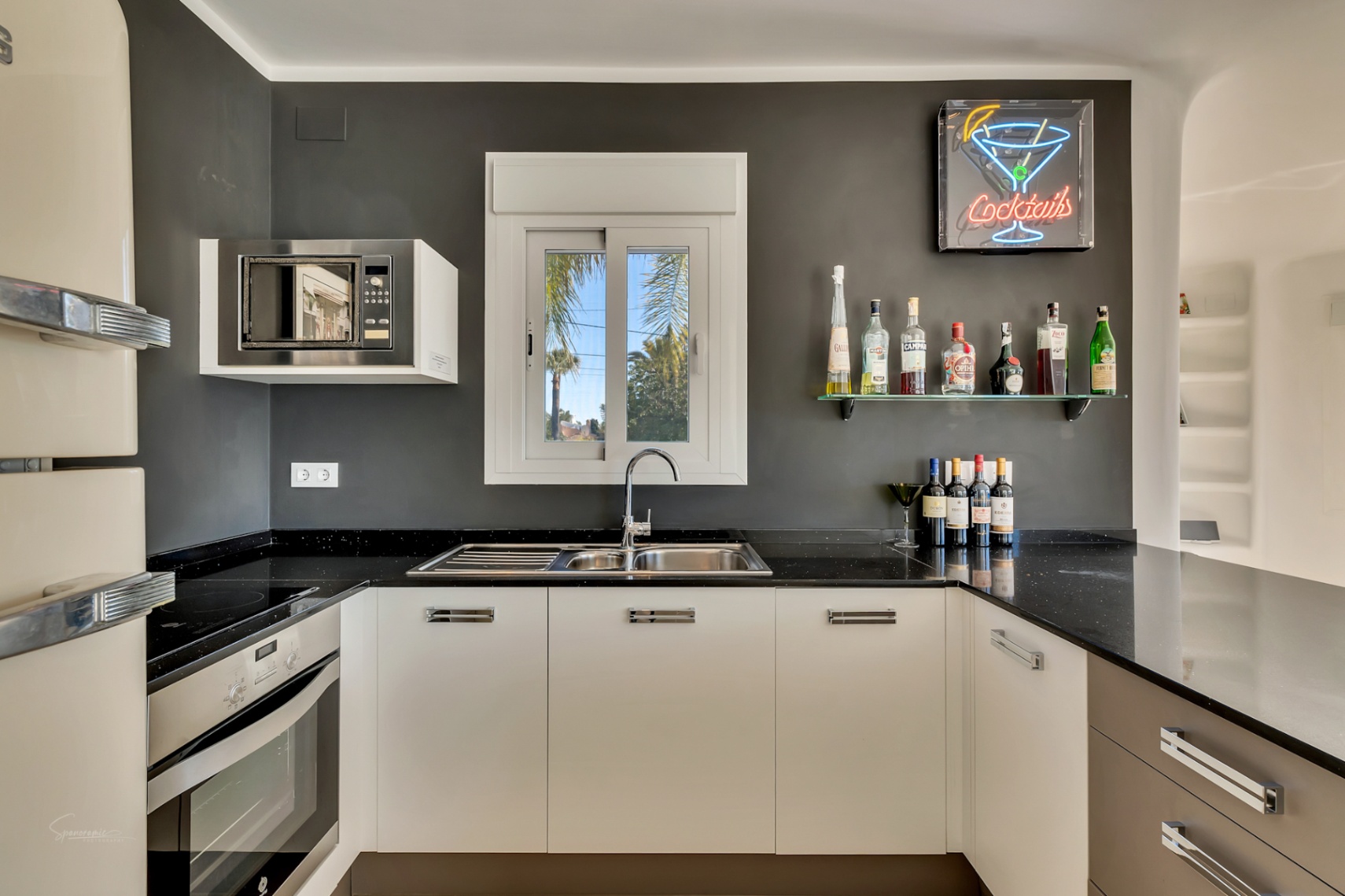 Moderne keuken met zwart granieten aanrechtblad, antracietgrijze muren en een barhoek voorzien van een glazen planchet en neonreclame.