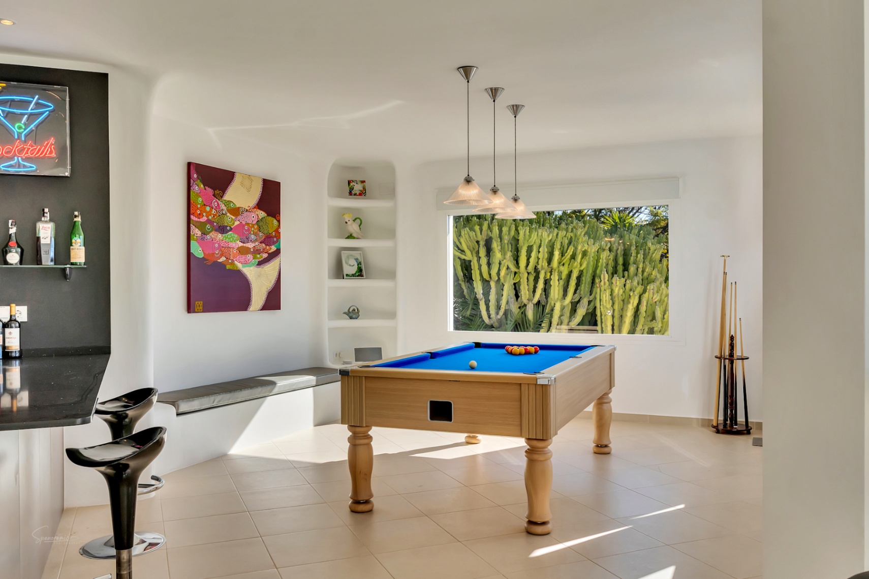 Ontspanningsruimte in Ibiza-stijl met een professionele biljarttafel, bar en een groot raam met uitzicht op een cactustuin. Voorzien van witte organische muren en moderne verlichting.