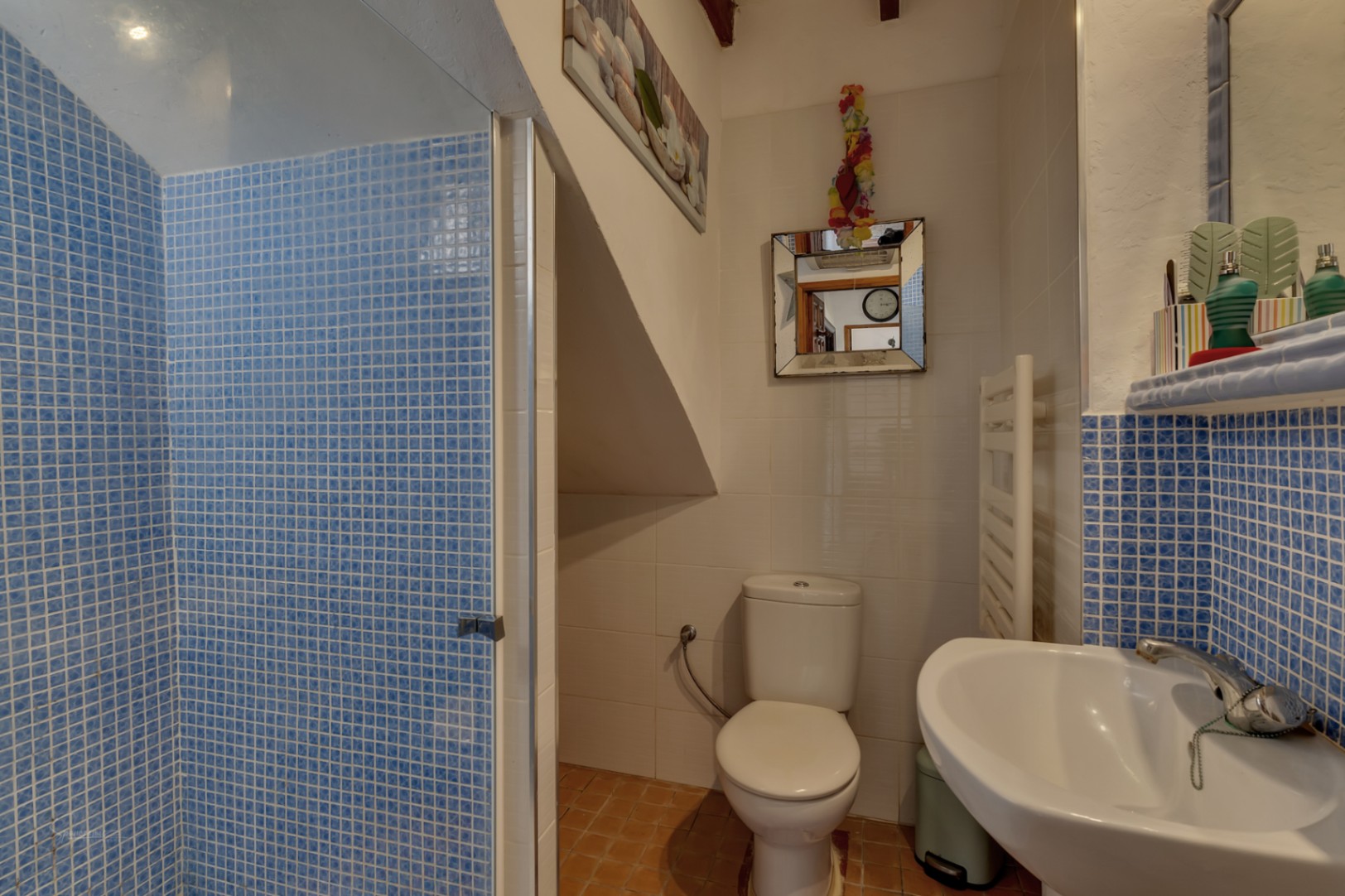 Badkamerdetail met blauwe mozaïekdouche, wit toilet en wastafel met mozaïekblad.