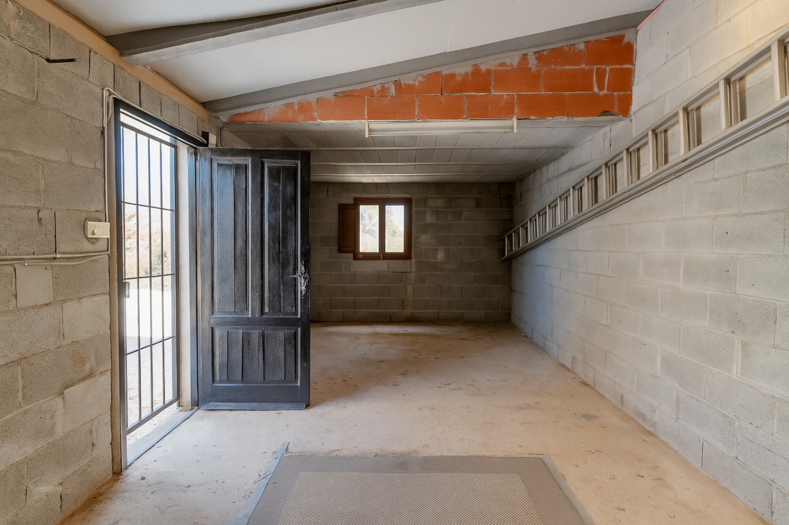 Garage-interieur met betonblokwanden, open houten deur en metalen ladder.
