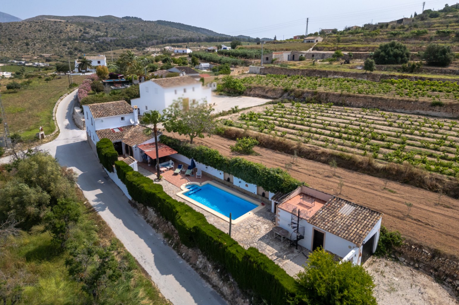 Luchtfoto van een finca met blauw zwembad, volgroeide tuin en velden in Teulada, Costa Blanca.