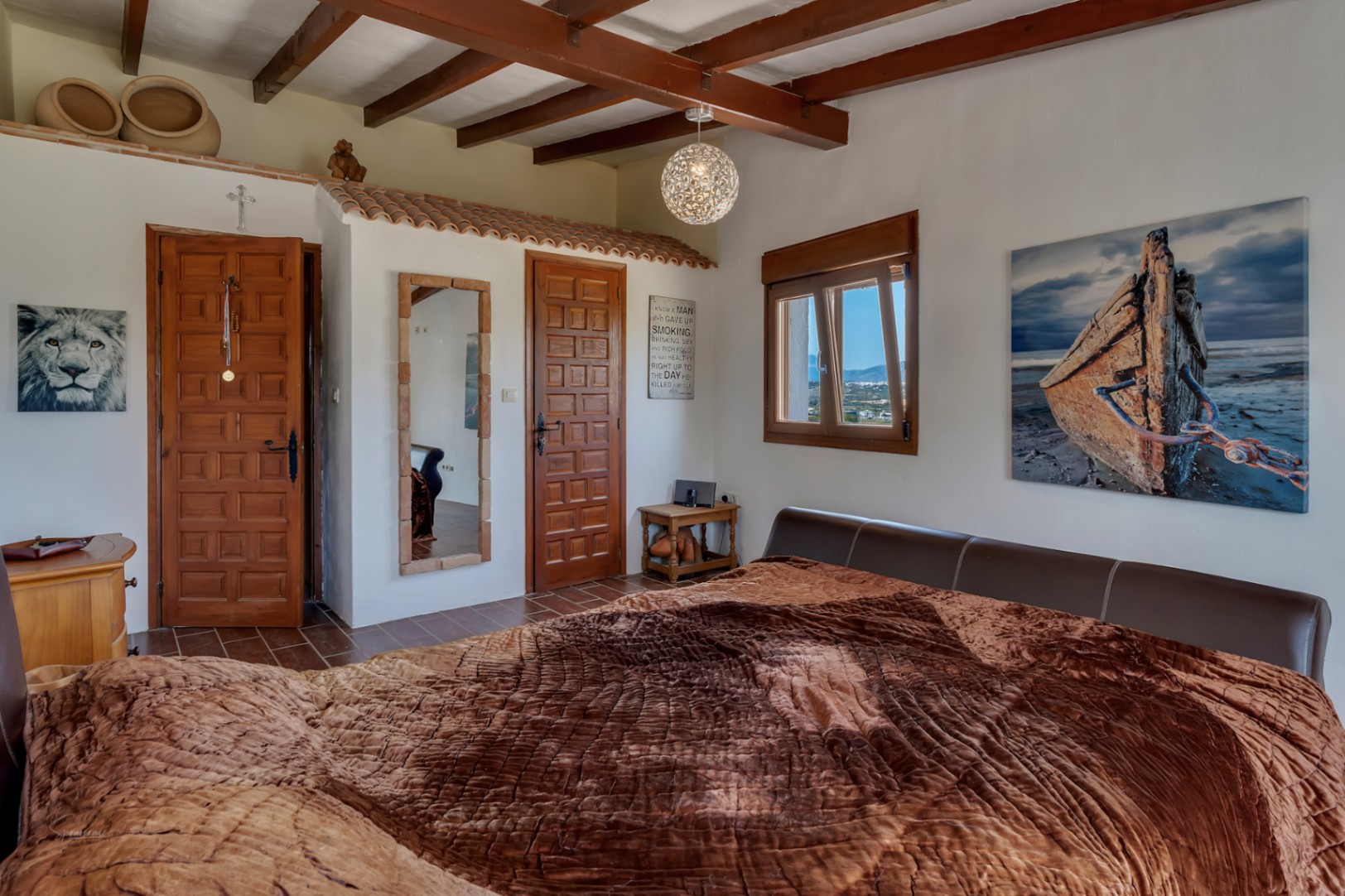 Rustieke slaapkamer met houten balken, tegelvloer en een bed met een bruin lederen hoofdeinde.