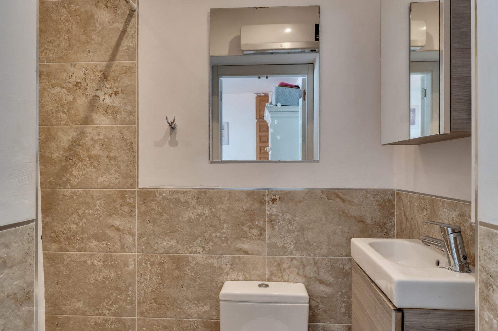 Badkamerdetail met crèmekleurige tegels en een spiegel die een andere kamer reflecteert.