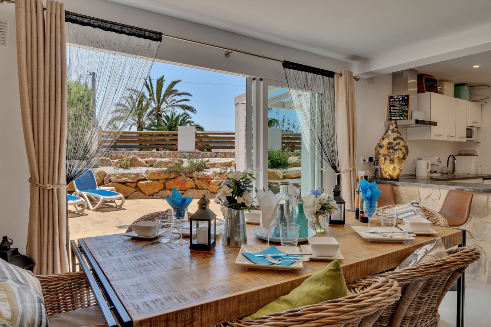 Lichte eetkamer met rustieke tafel en toegang tot terras met ligstoelen en mediterrane tuin.