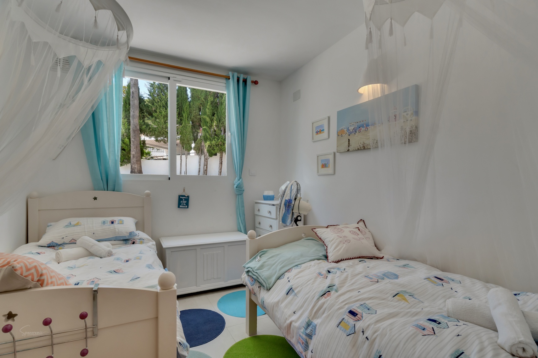 Lichte kinderkamer met twee eenpersoonsbedden, decoratie met strandthema en uitzicht naar buiten.