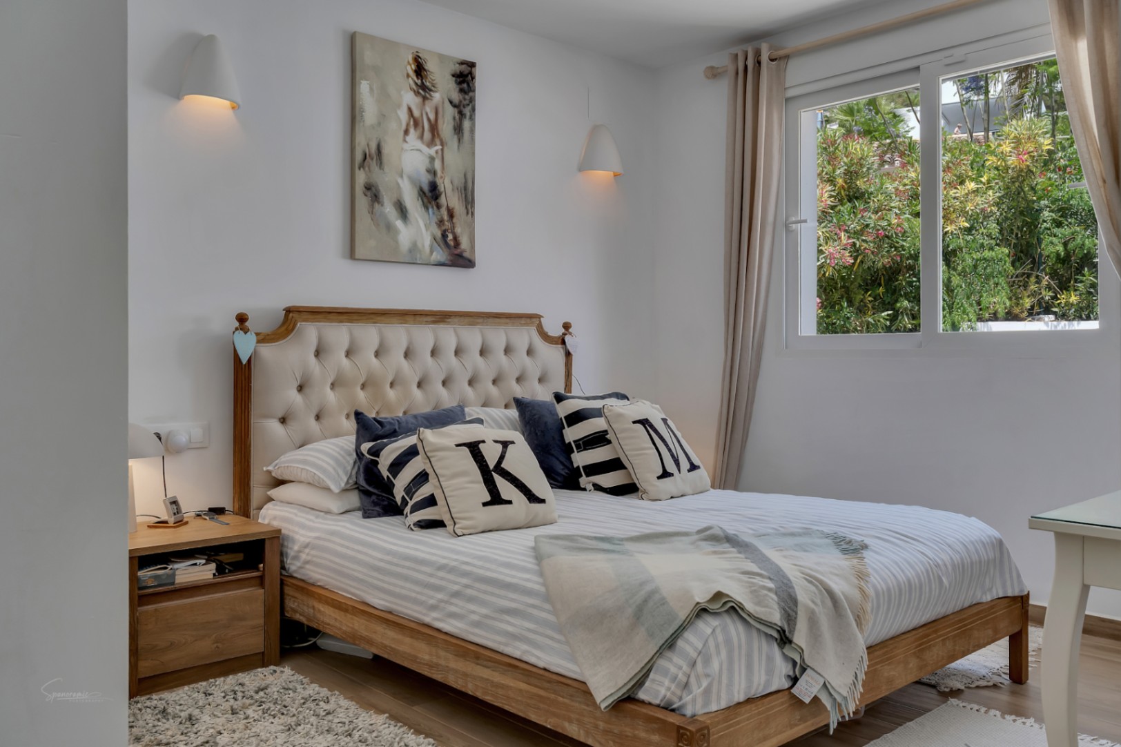 Lichte slaapkamer met houten bed en gestoffeerd hoofdeinde. Neutrale inrichting en natuurlijk licht.