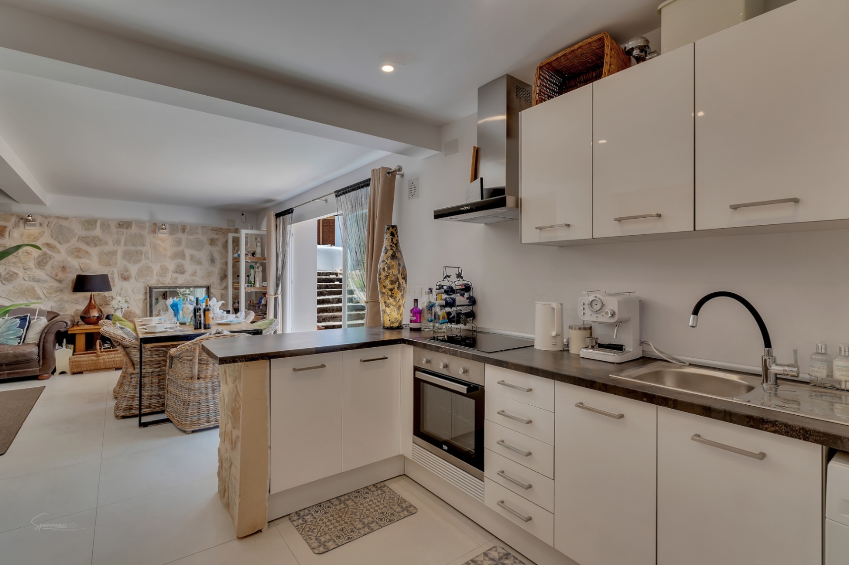 Open keuken met donkere werkbladen en uitzicht op eetkamer met stenen muur.