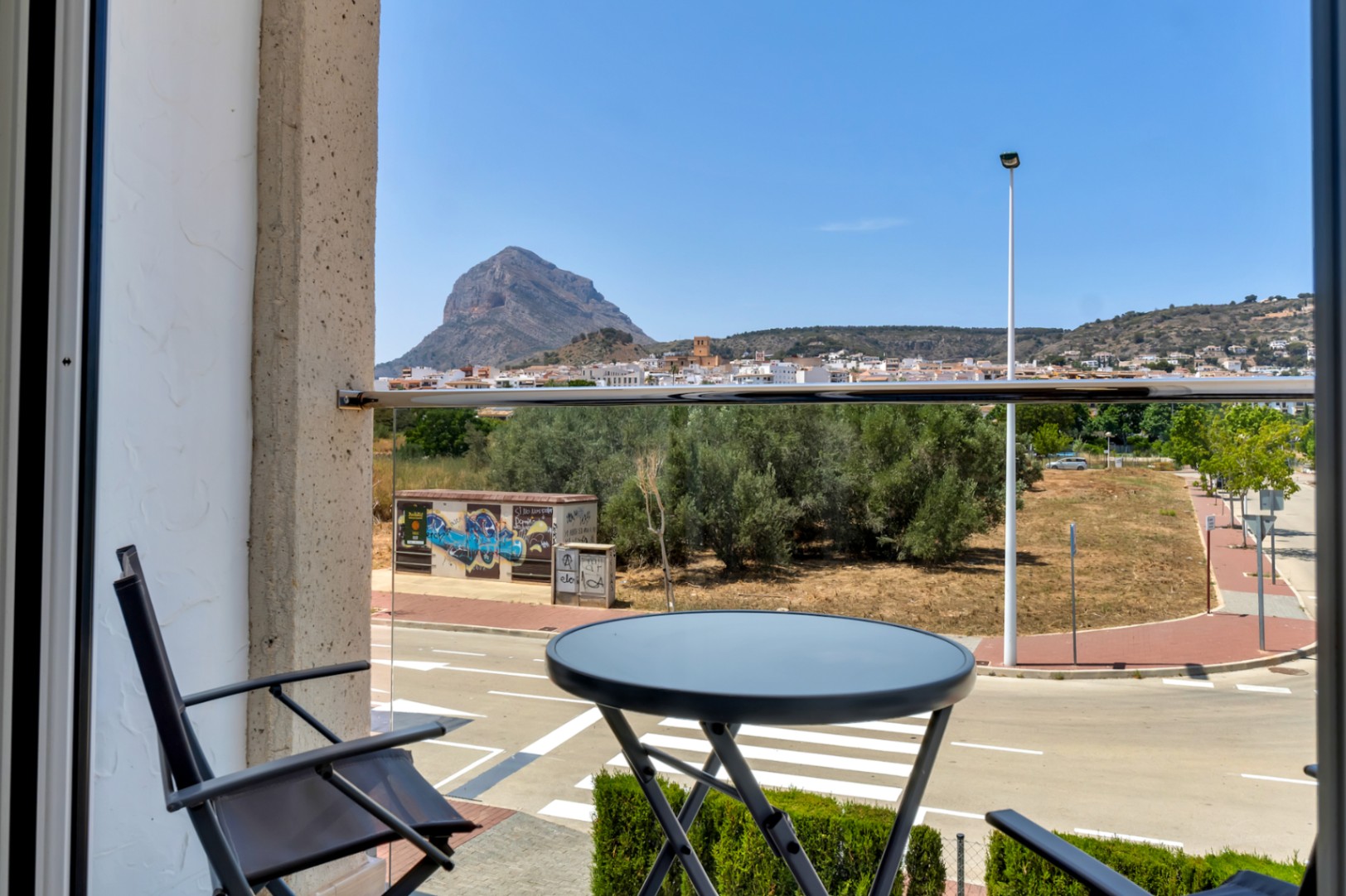 Balkon met glazen balustrade en bistroset, met een weids uitzicht op de berg Montgó en het historische centrum van Jávea.